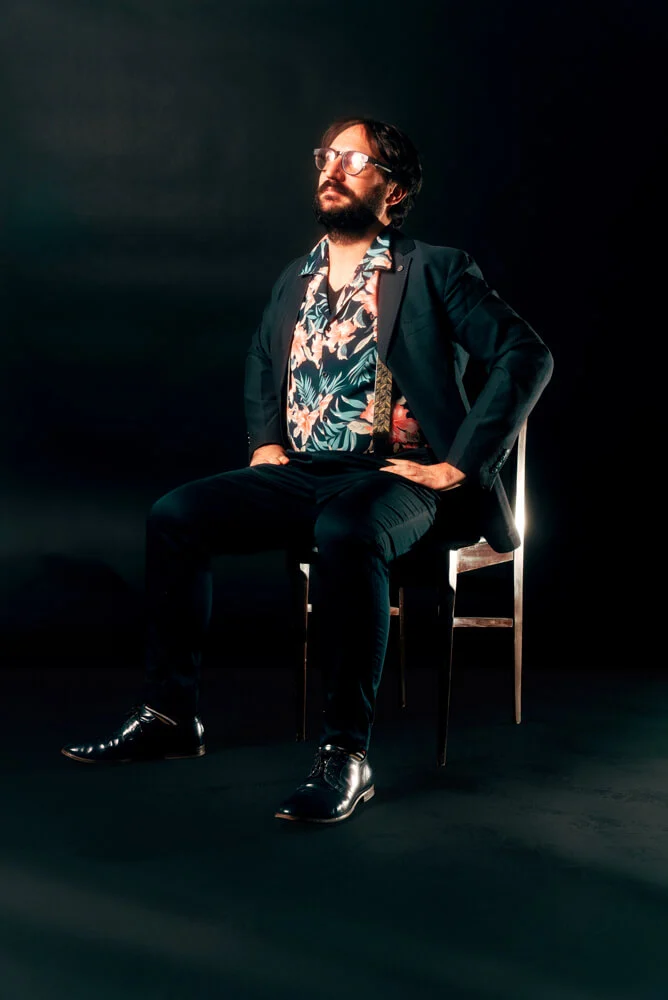 One of our designer seated on a chair against a black background