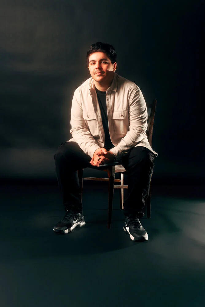 One of our designer seated on a chair against a black background