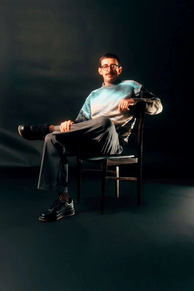 Our co-founder and design director, seated on a chair against a black background